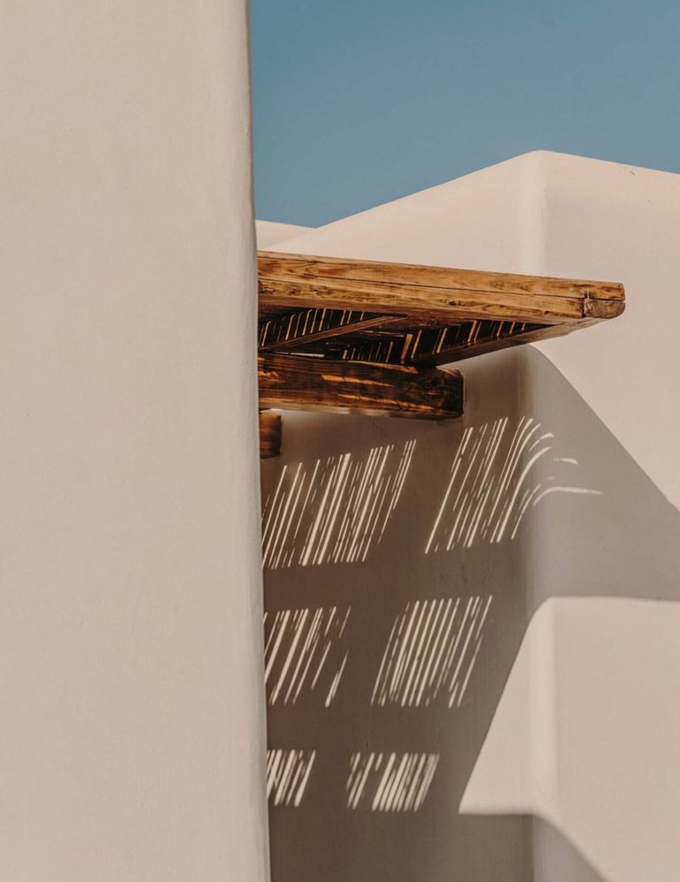 Wooden beam attached to white building wall with blue sky and sharp shadow pattern cast on the white surface