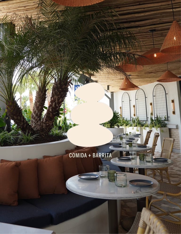 Modern restaurant dining area with marble tables, rust-colored pendant lights, potted palm trees, and upholstered seating under wooden ceiling